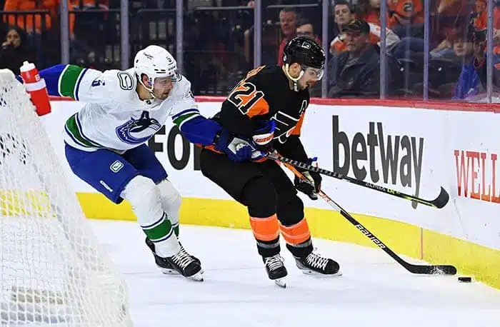Vancouver Canucks defenseman Tucker Poolman (5) reaches across Philadelphia Flyers left wing Scott Laughton (21) as he collects the puck in the first period at Wells Fargo Center.